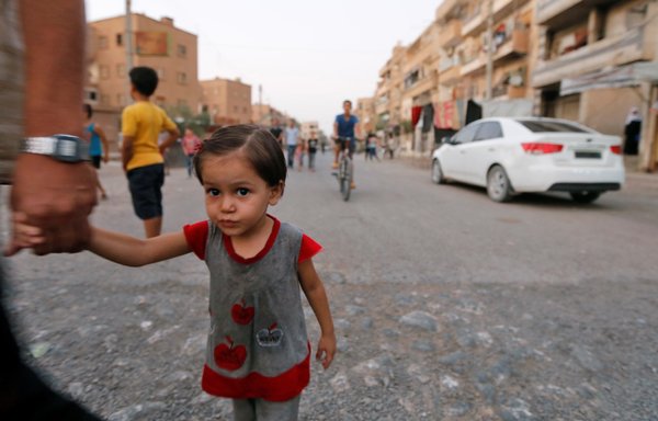 A Syrian man holds the hand of a child as civilians are seen on a street in the eastern city of Deir Ezzor in this file photo from September 20, 2017. [Louai Beshara/AFP]