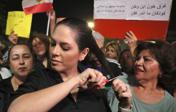 A demonstrator cuts a lock of her hair during a gathering by Israelis of Iranian origin in support of Iranian protests in Tel Aviv on October 29. [Jack Guez/AFP]