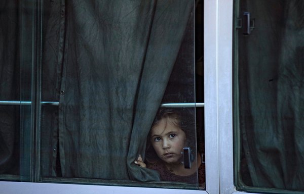 A child peers out of a bus full of women and children from families of ISIS fighters after Kurdish authorities in Syria handed them over to Tajikistan in 2022. [Delil SOULEIMAN / AFP]