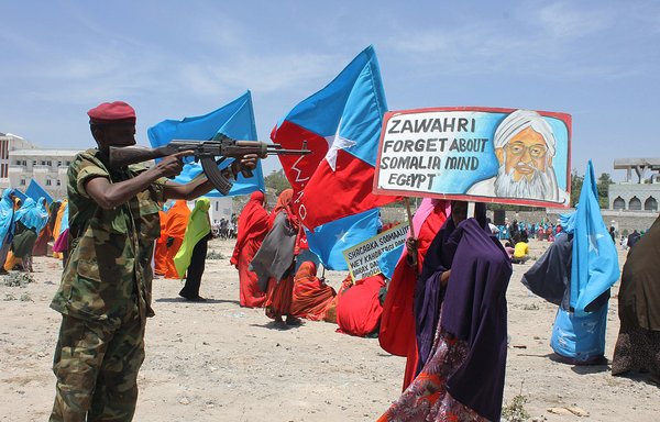 In this file photo from February 2014, a Somali soldier points his weapon at a poster bearing a photo of then al-Qaeda leader Ayman al-Zawahiri during an anti al-Shabaab rally in Mogadishu. [Abdifitah Hashi Nor/AFP]