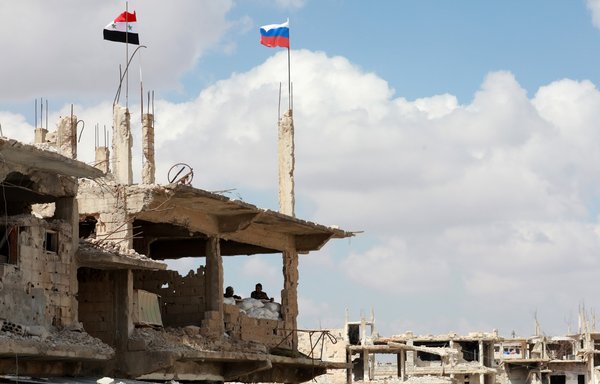 A picture taken during a tour organised by the Syrian Ministry of Information in September 2021 shows Syrian and Russian flags flying above a damaged building in the district of Daraa al-Balad in Daraa, Syria. [Louai Beshara/AFP]